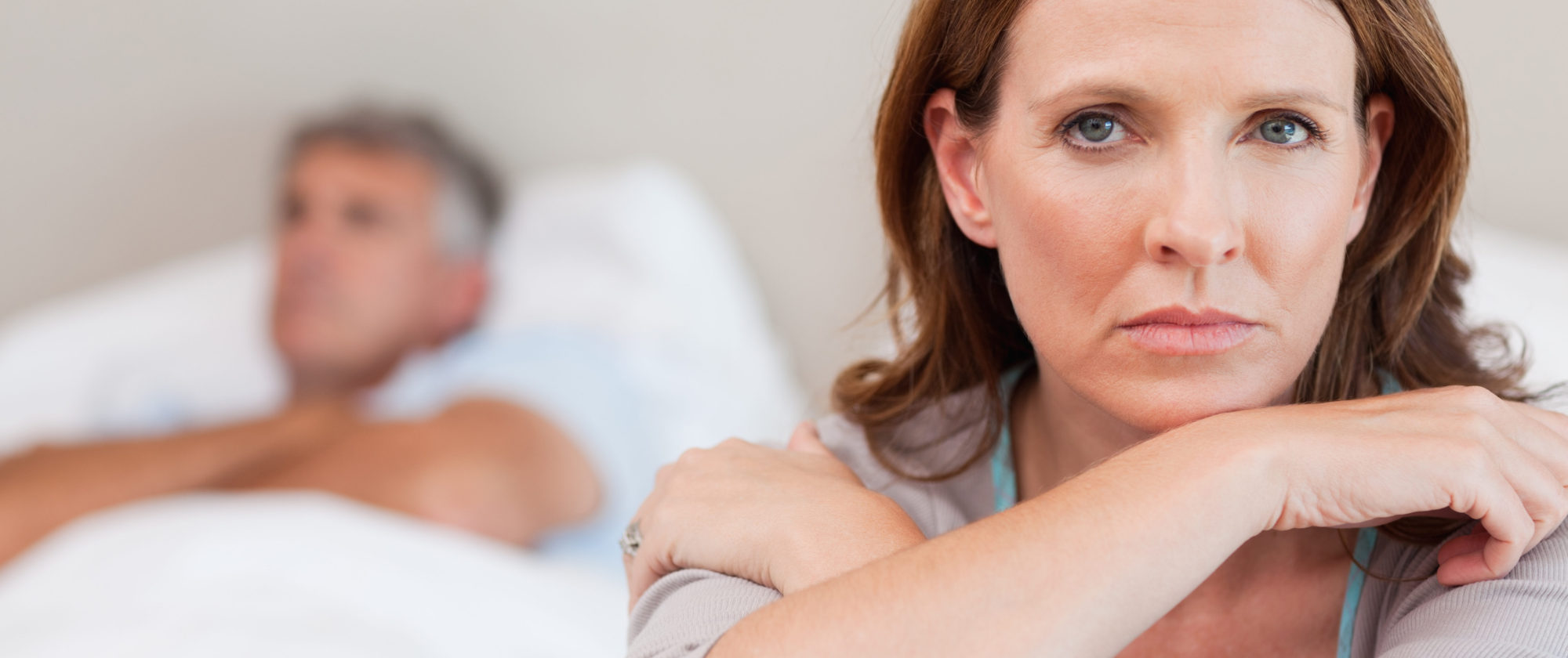 Sad woman on the bed with her husband in the background